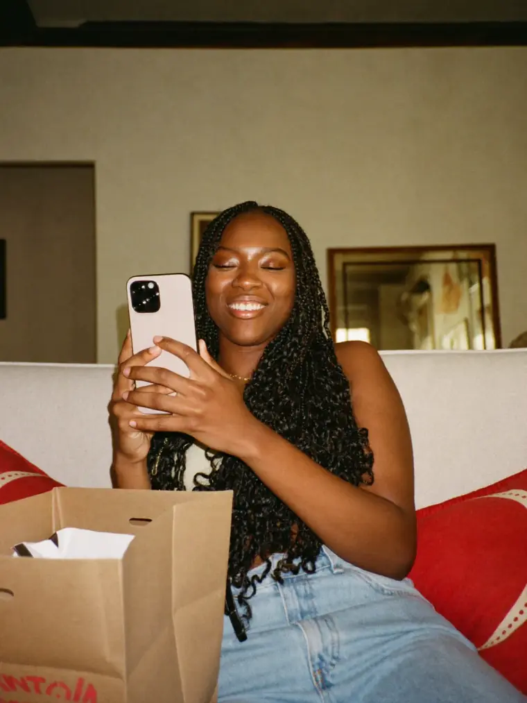 Cliente sorrindo no sofá de casa, escolhendo peças pelo celular