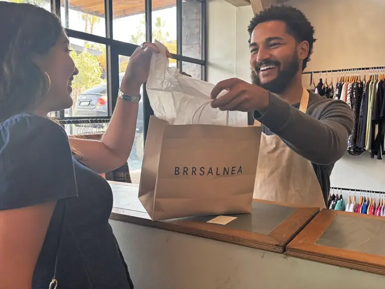 Lojista entregando a sacola de compra para uma cliente feliz no balcão